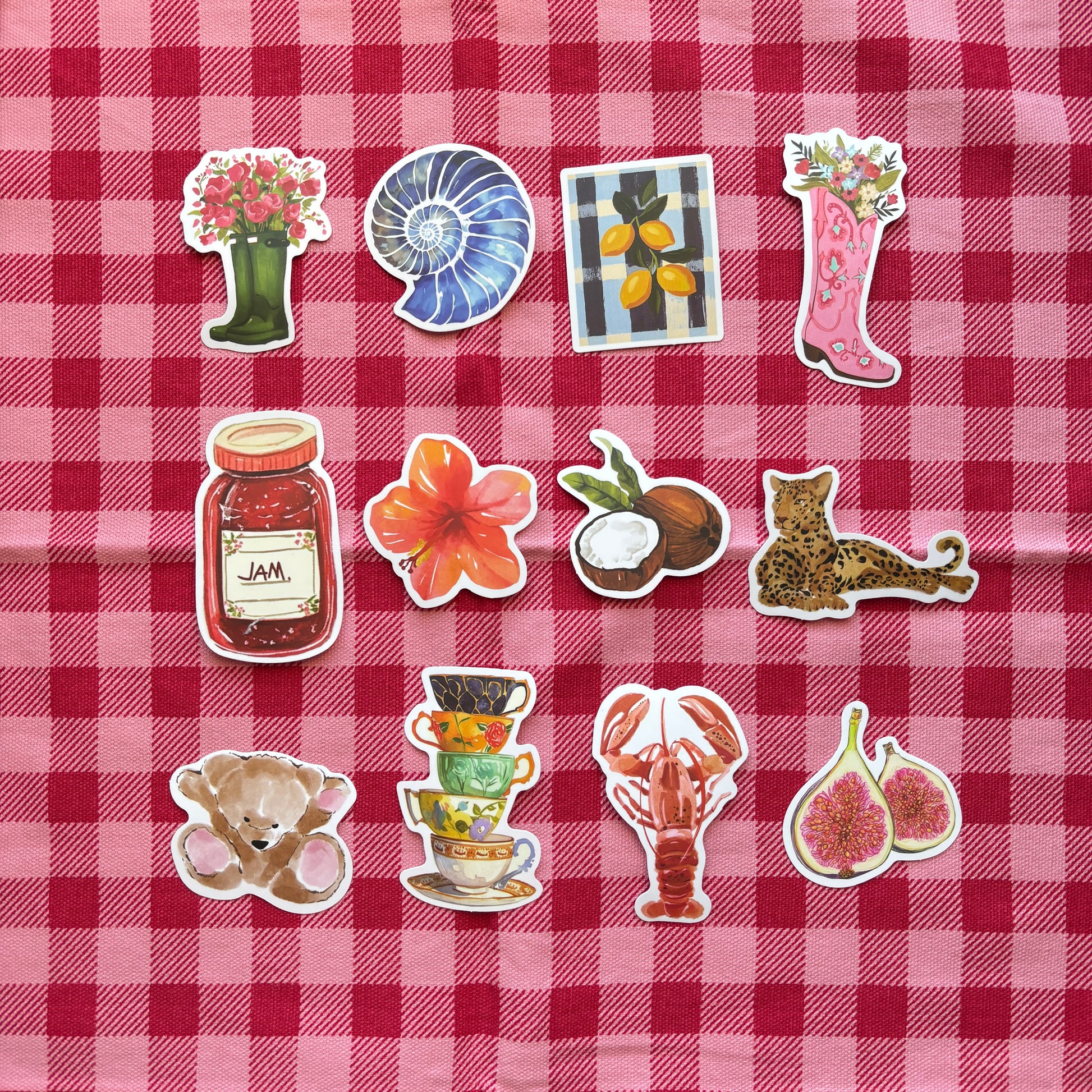 Decorative scrap journal stickers including flowers, fruit, animals, and objects arranged on red gingham fabric